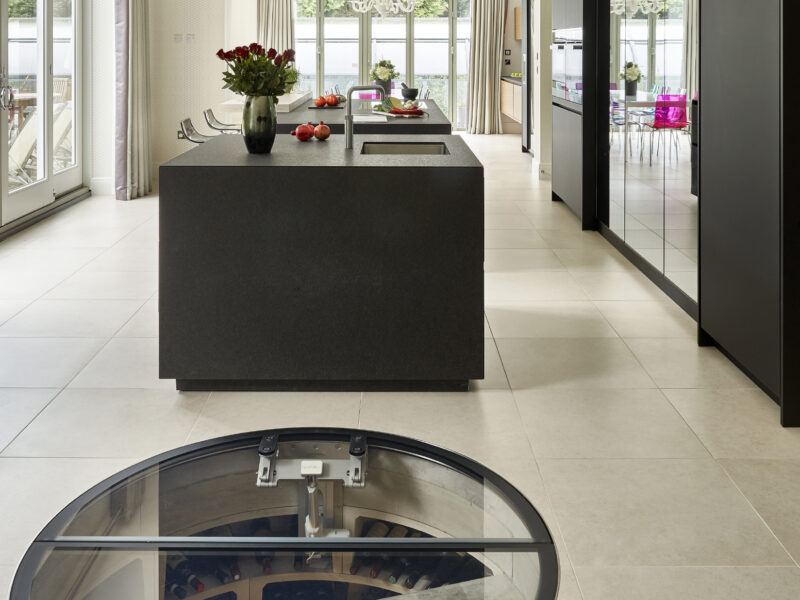 London kitchen with modern fridge, glass cabinet, and oven with timber cabinets and a white kitchen table with different coloured chairs wine cellar