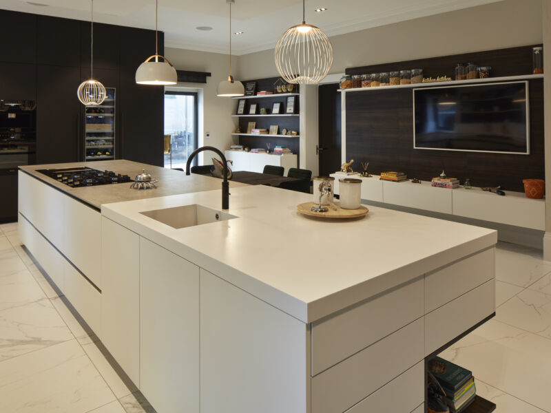 Modern, black and white kitchen with drop lights and hidden storage and a wine fridge with tv unit and dining area