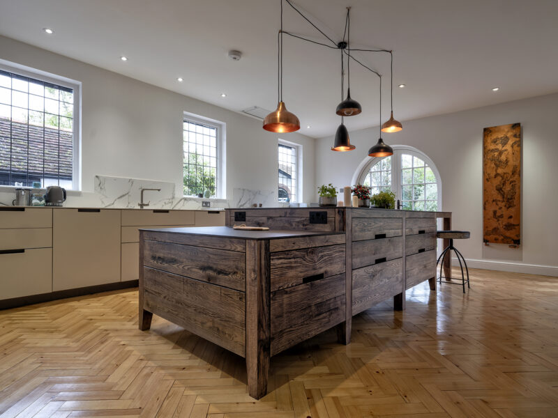 Large kitchen design with herringbone flooring and kitchen islands and floating log burner