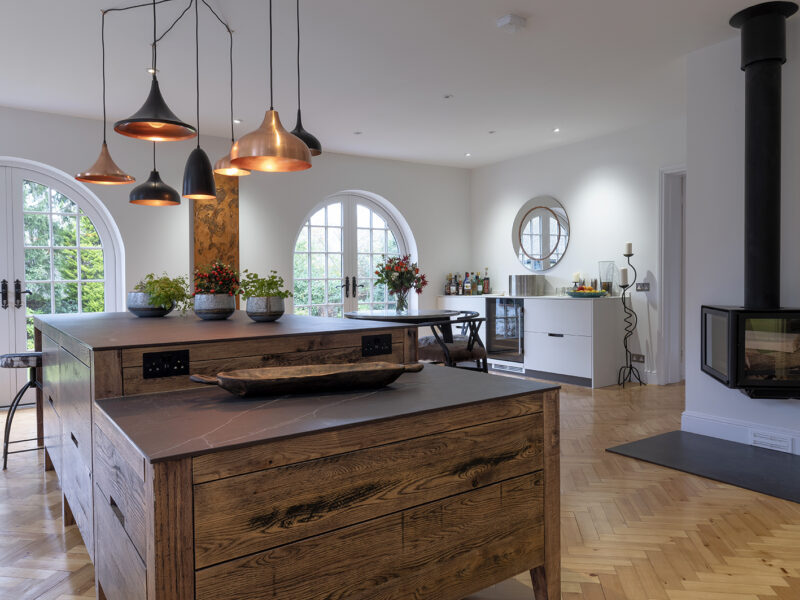 Large kitchen design with herringbone flooring and kitchen islands and floating log burner