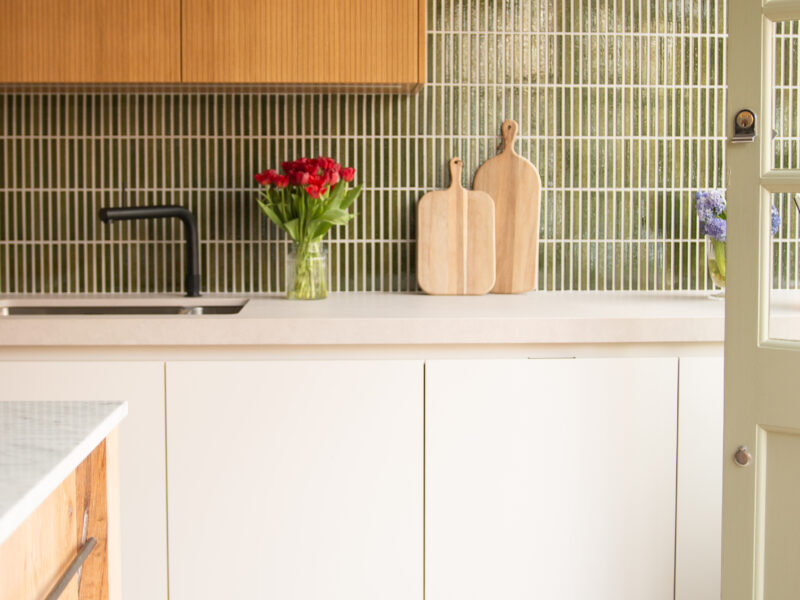 Modern kitchen with wooden cabinets, white countertops and vase with red flowers